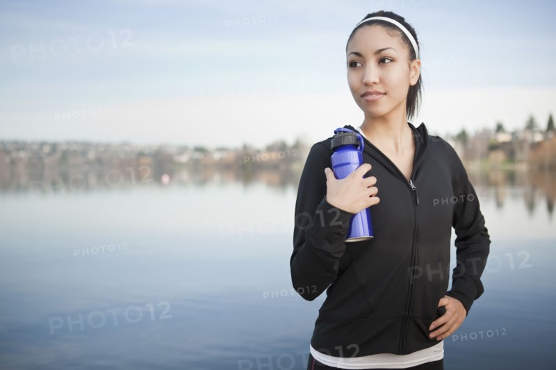Mixed race woman near lake holding water bottle