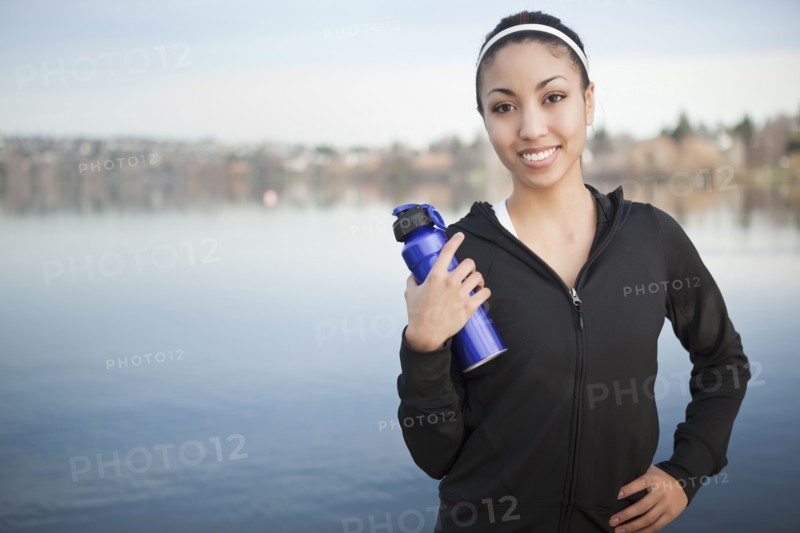Mixed race woman near lake holding water bottle