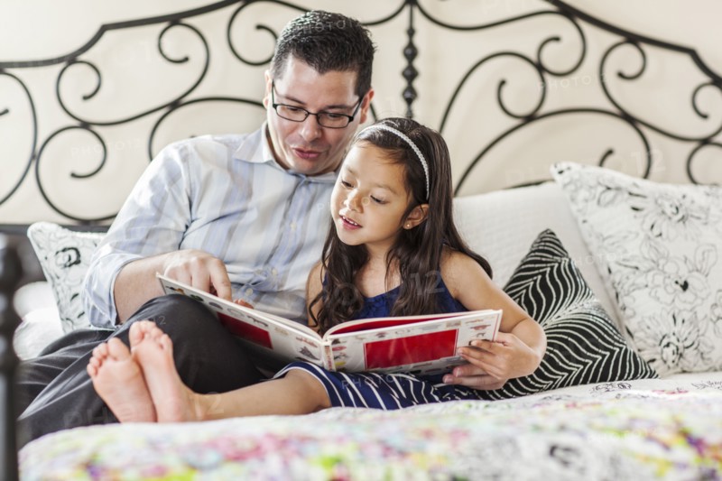 Father reading to daughter on bed