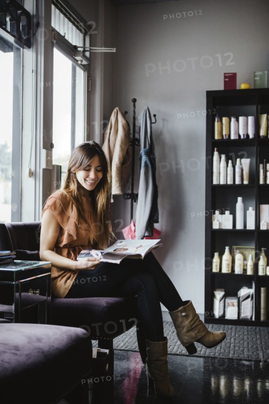 Mixed race woman reading magazine in salon