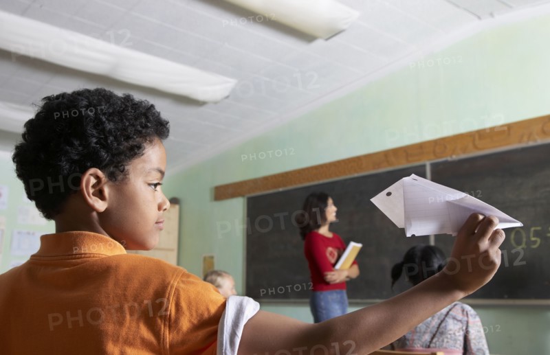Mixed Race boy throwing paper airplane in class