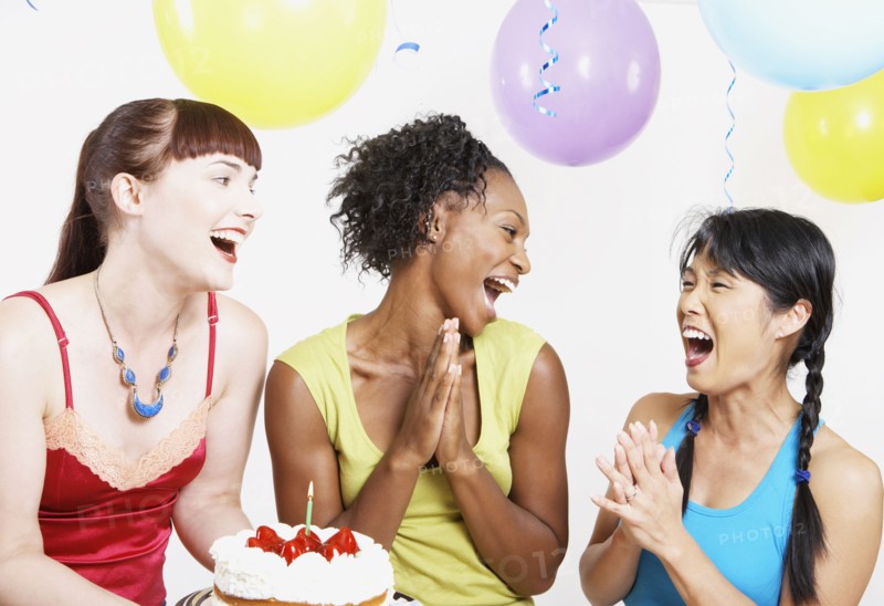Three women laughing with cake at party