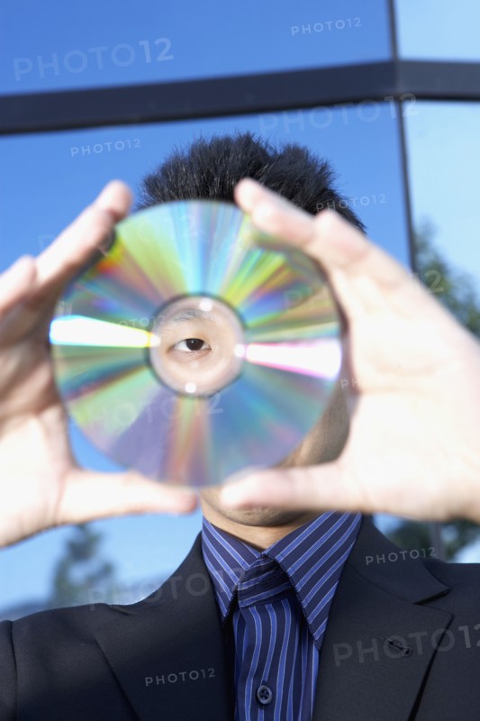 Asian businessman looking through center of cd