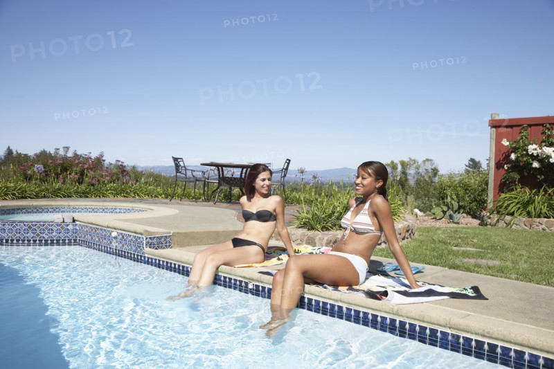 Multi-ethnic women with feet in swimming pool