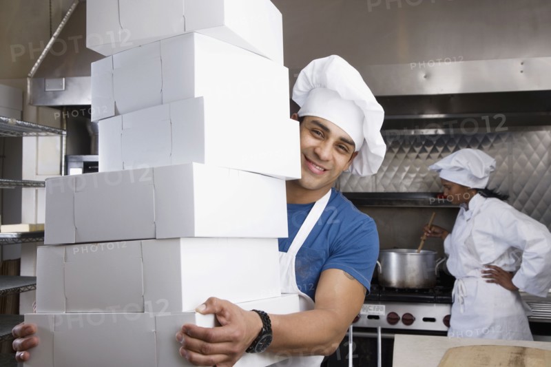 Hispanic male pastry chef carrying stack of boxes
