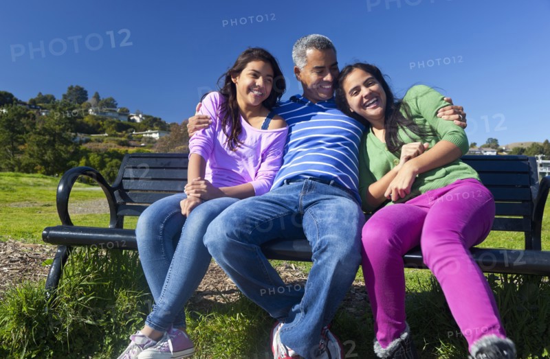 Hispanic father and daughters sitting on park bench