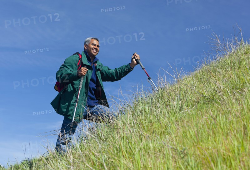 Mixed race man hiking on grassy hill