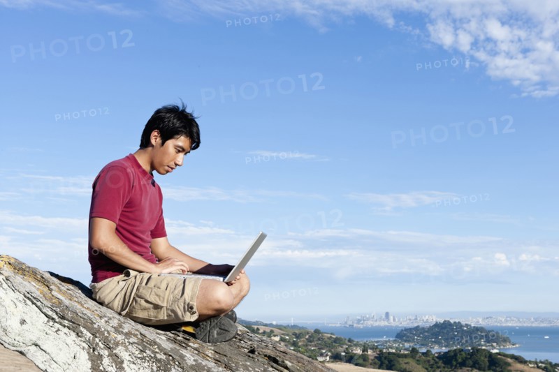 Climber using laptop on rocky hilltop