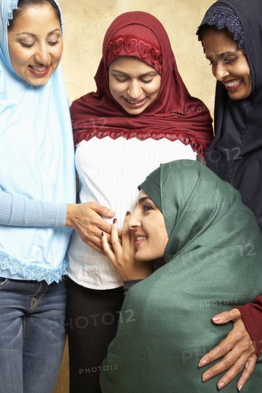 Woman in headscarf listening to friend's pregnant belly