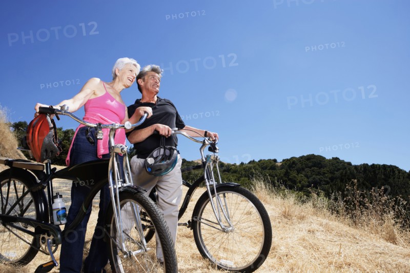 Senior Caucasian couple wheeling dirt bikes on hilltop