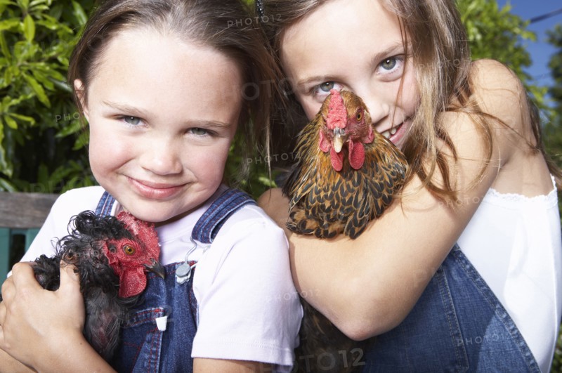 Mixed race girls holding chickens on farm
