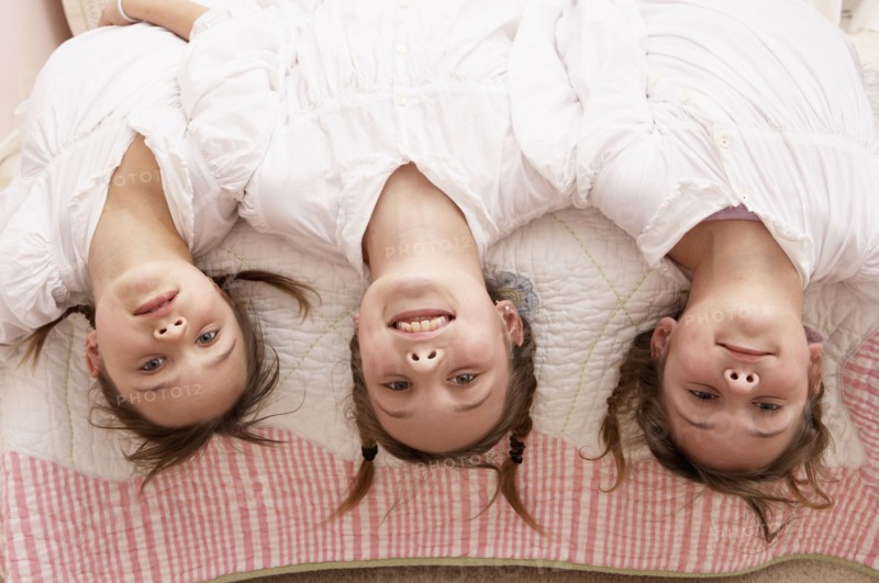 Mixed race girls hanging upside down from bed