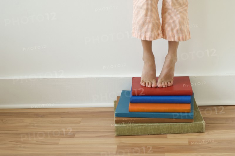 Girl standing on tiptoes on stack of books