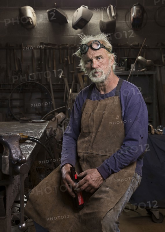 Portrait of serious Caucasian blacksmith in workshop drinking beer