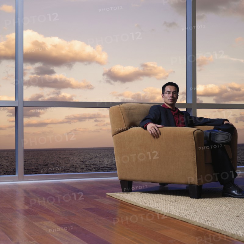 Asian man sitting next to window overlooking water