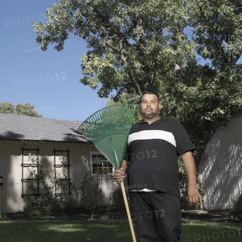 Hispanic man standing in yard with rake