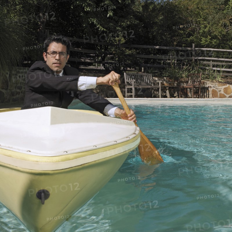 Mixed race businessman rowing boat in swimming pool