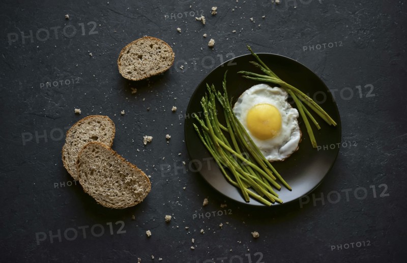 Bread and crumbs near plate with fried egg and asparagus
