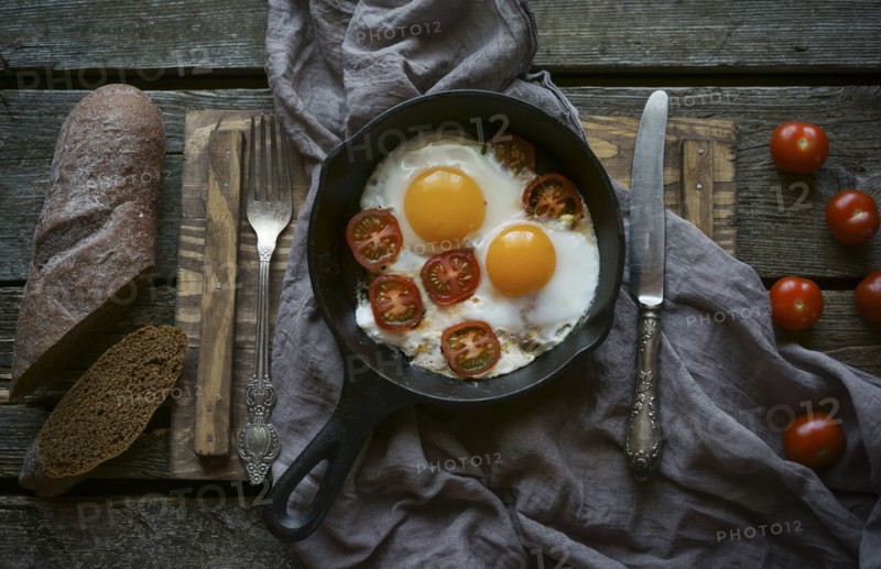Eggs and tomatoes in frying pan on wooden table