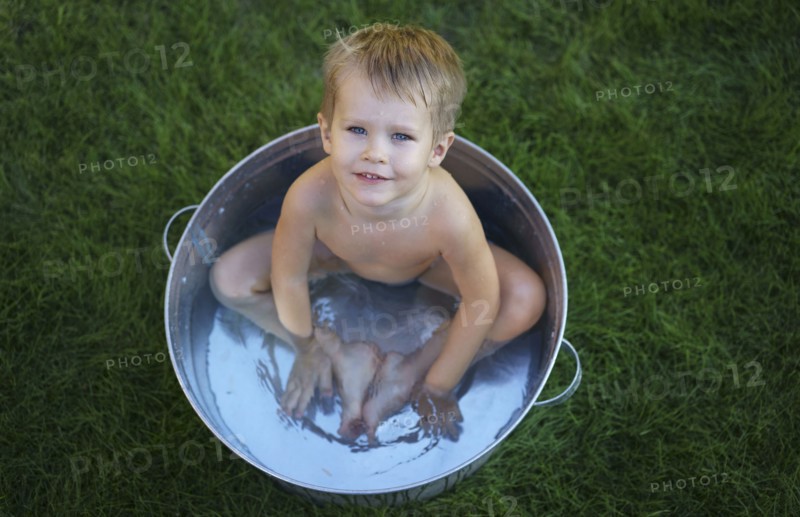 Naked Caucasian boy in metal tub in grass