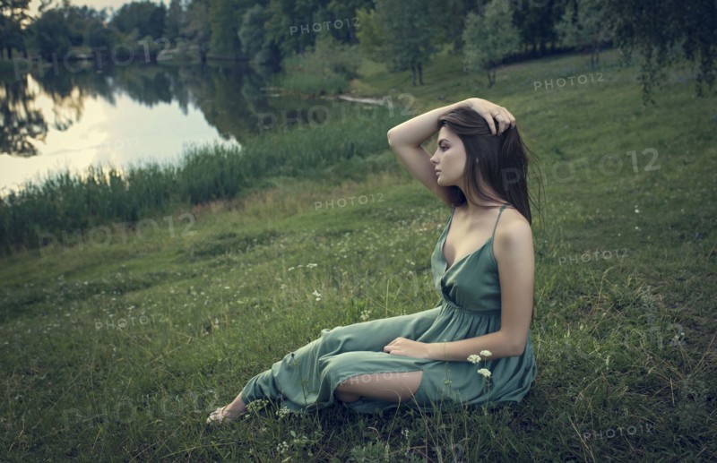 Caucasian woman sitting in grass with wildflowers near lake