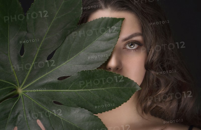 Caucasian woman hiding behind green leaf