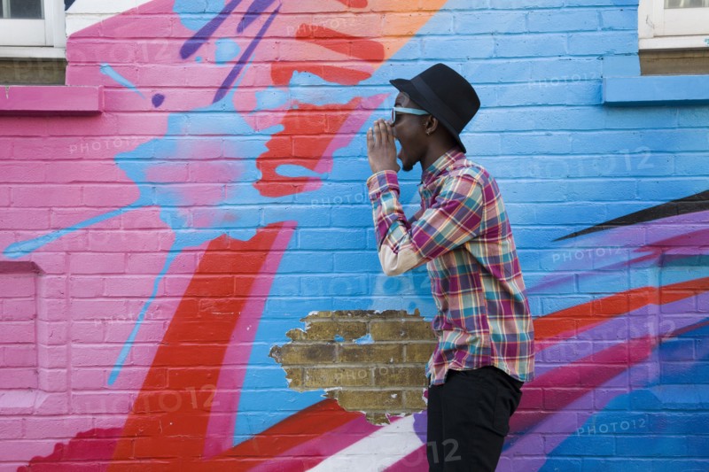 Black man in sunglasses shouting near colorful wall
