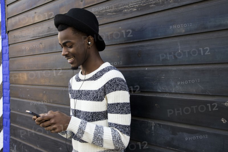 Black man listening to mp3 player near wooden wall