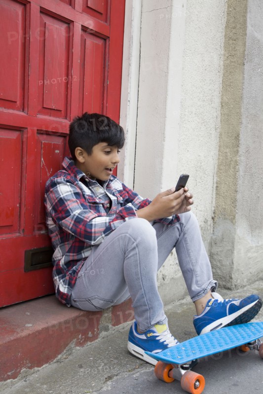 Asian boy with skateboard using cell phone