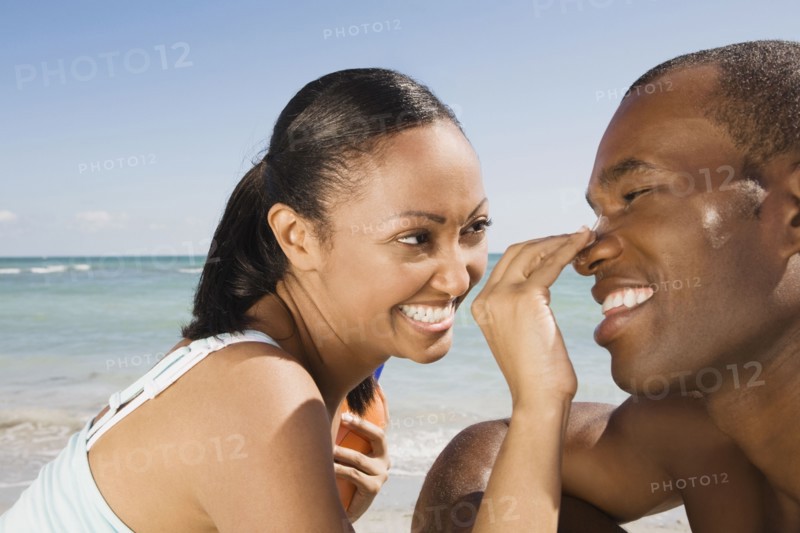 Hispanic woman rubbing sunscreen on boyfriend's nose