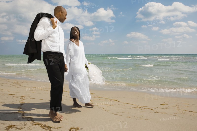 African bride and groom holding hands at beach