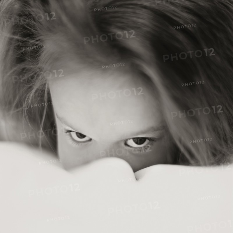 Caucasian girl peering over bed covers