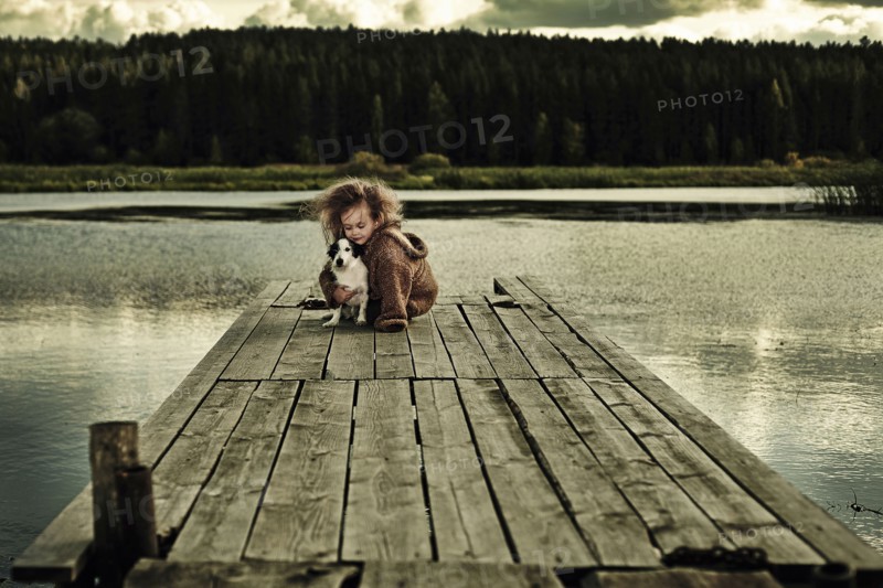 Caucasian girl with dog on wooden deck in still lake