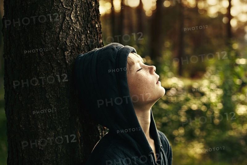 Caucasian boy leaning against tree