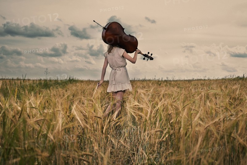 Caucasian girl carrying cello on shoulder in rural fieldCaption