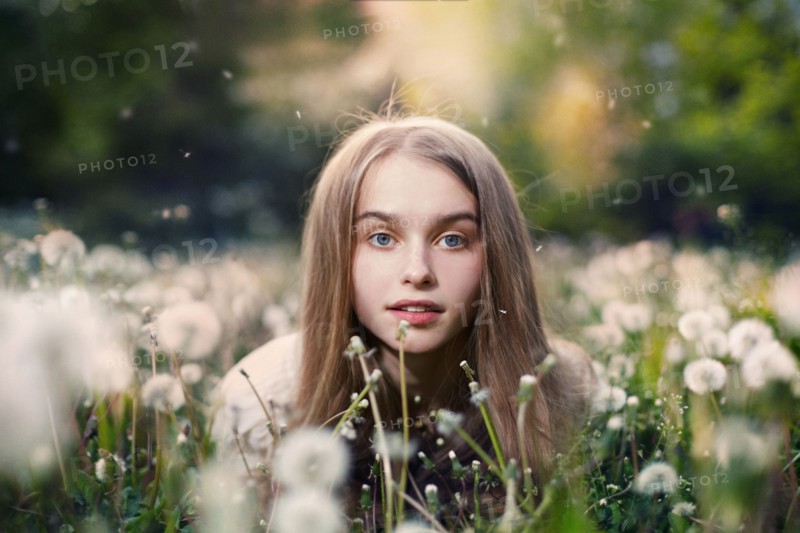 Caucasian girl laying in tall grass and dandelions