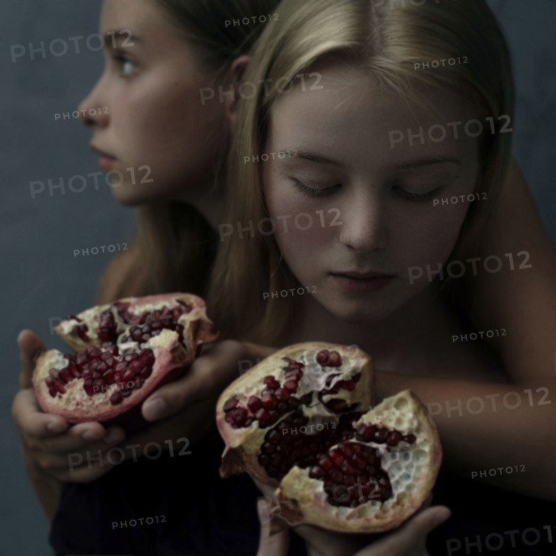 Intertwined Caucasian girls holding sliced pomegranate