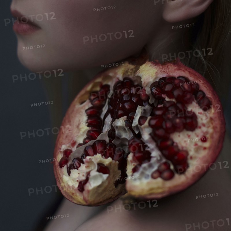 Caucasian girl balancing pomegranate slice on shoulder