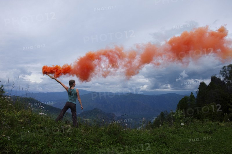Caucasian girl holding orange smoke flare on mountain range