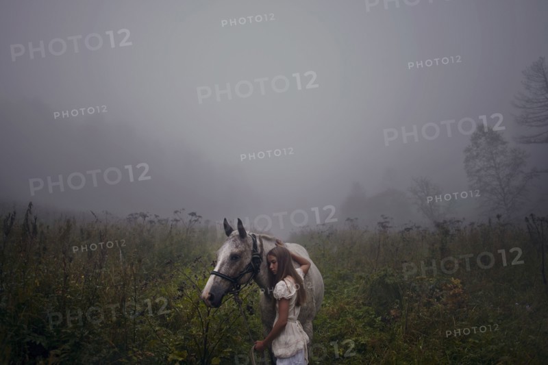 Caucasian girl petting horse in foggy field