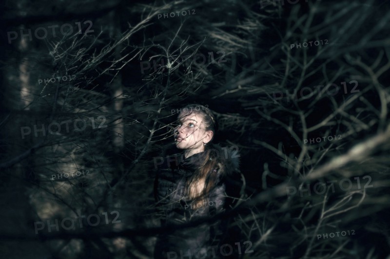 Caucasian teenage girl behind tree branches at night