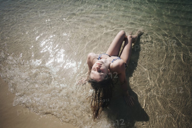 Caucasian woman wearing bikini sitting in waves on beach