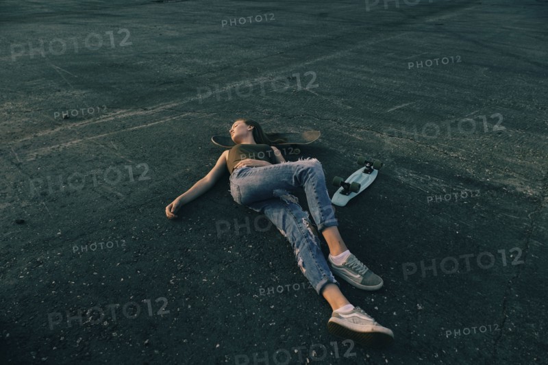Caucasian teenage girl laying on pavement with head on skateboard