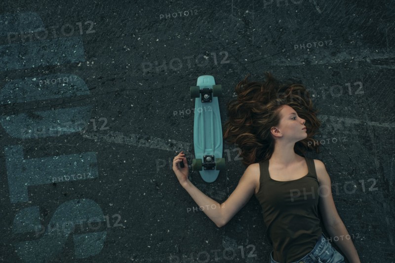 Caucasian teenage girl laying on pavement with skateboard