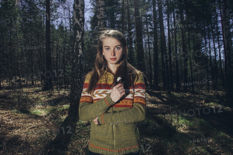 Serious Caucasian woman holding flower in forest