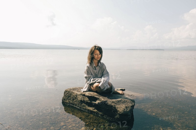 Caucasian girl sitting on rock in lake