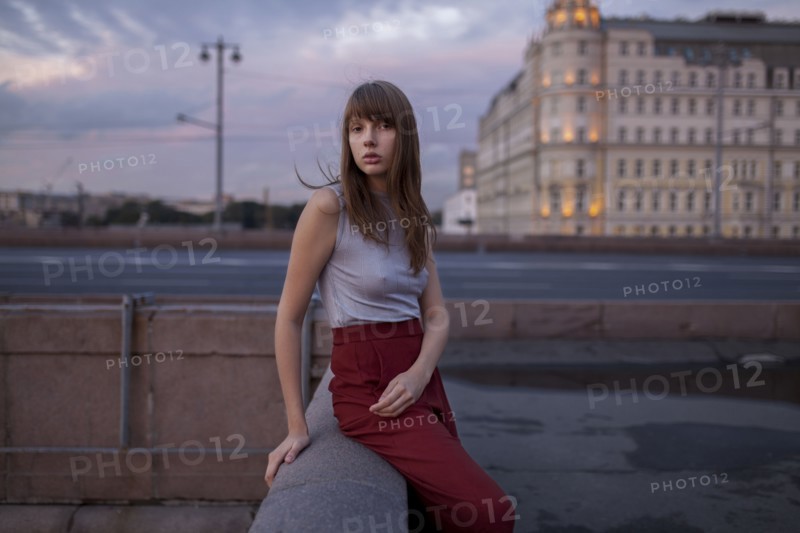 Serious Caucasian woman sitting on wall in city