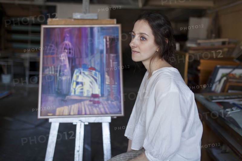 Caucasian artist sitting near paintings