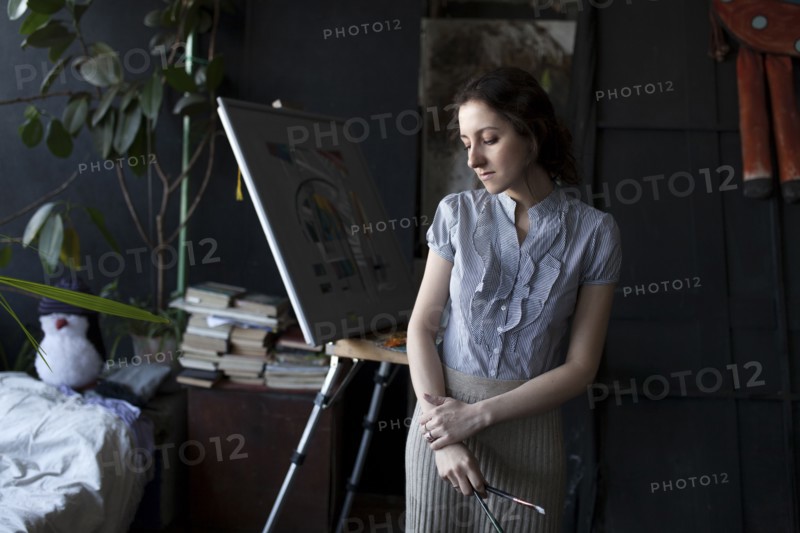 Pensive Caucasian artist holding paintbrushes