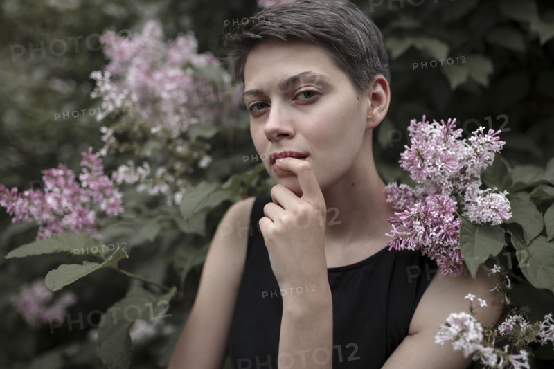 Curious Caucasian woman near flowering tree with finger on lip